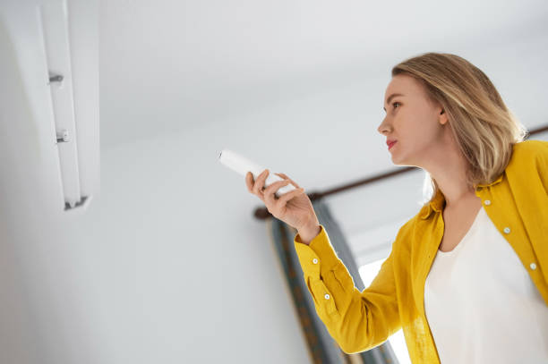 istock Woman holding remote control aimed at the air conditioner. 1368396337