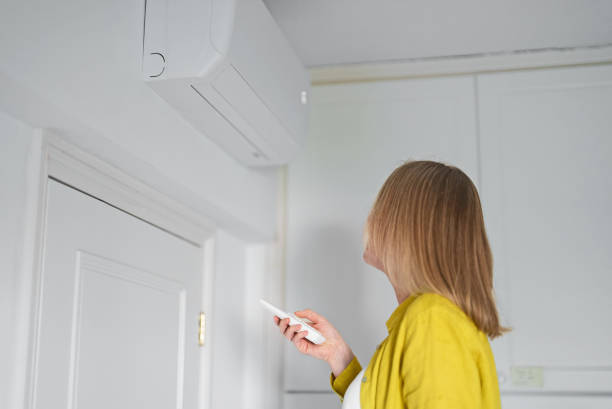 istock Woman holding remote control aimed at the air conditioner. 1368396345