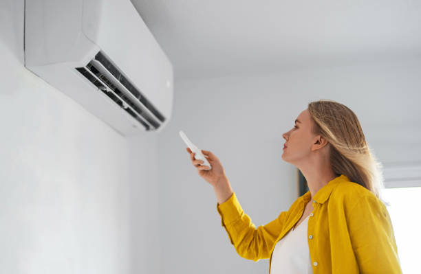 Woman holding remote control aimed at the air conditioner. stock photo