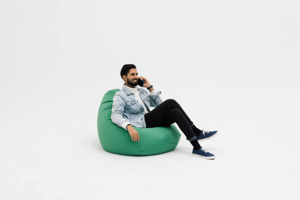 istock Young man sit in bag chair talk speak on mobile cell phone spread arm rest relax isolated on white background 1368397607
