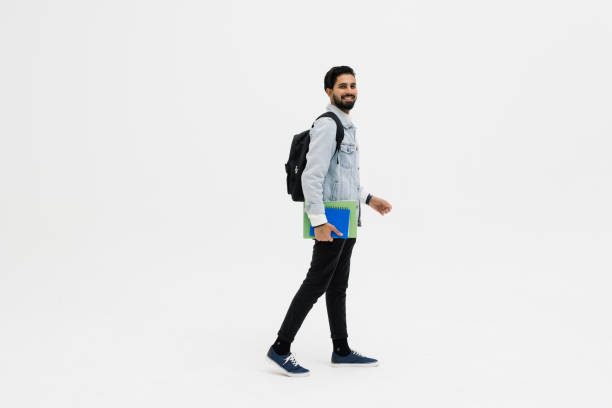 istock Young student indian man smiling, looking at camera and holding books walk isolated on white background 1368397646