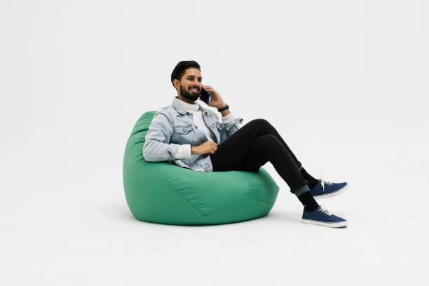 istock Young man sit in bag chair talk speak on mobile cell phone spread arm rest relax isolated on white background 1368397708