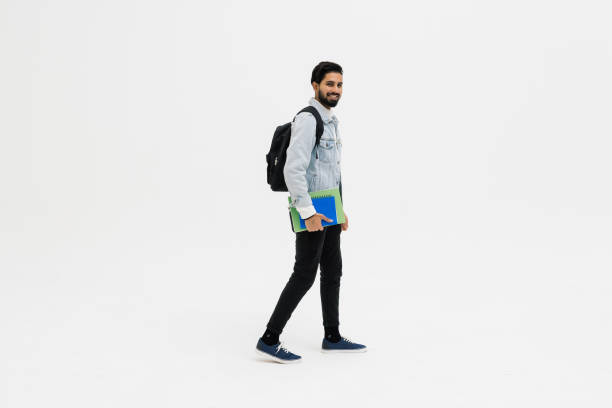 istock Young student indian man smiling, looking at camera and holding books walk isolated on white background 1368397945
