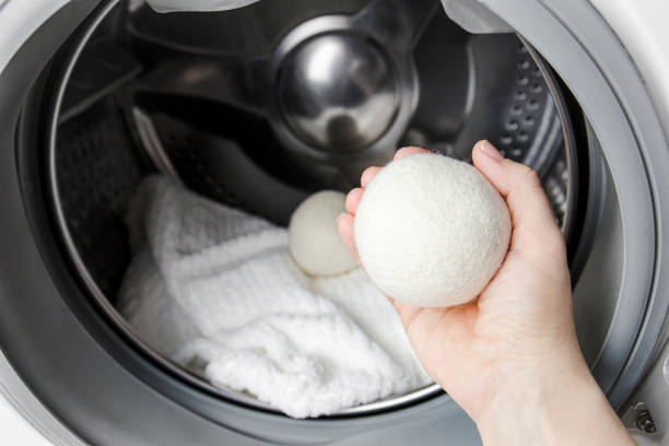 woman using wool dryer balls for more soft clothes while tumble drying in washing machine concept. discharge static electricity and shorten drying time, save energy. - wol stockfoto's en -beelden