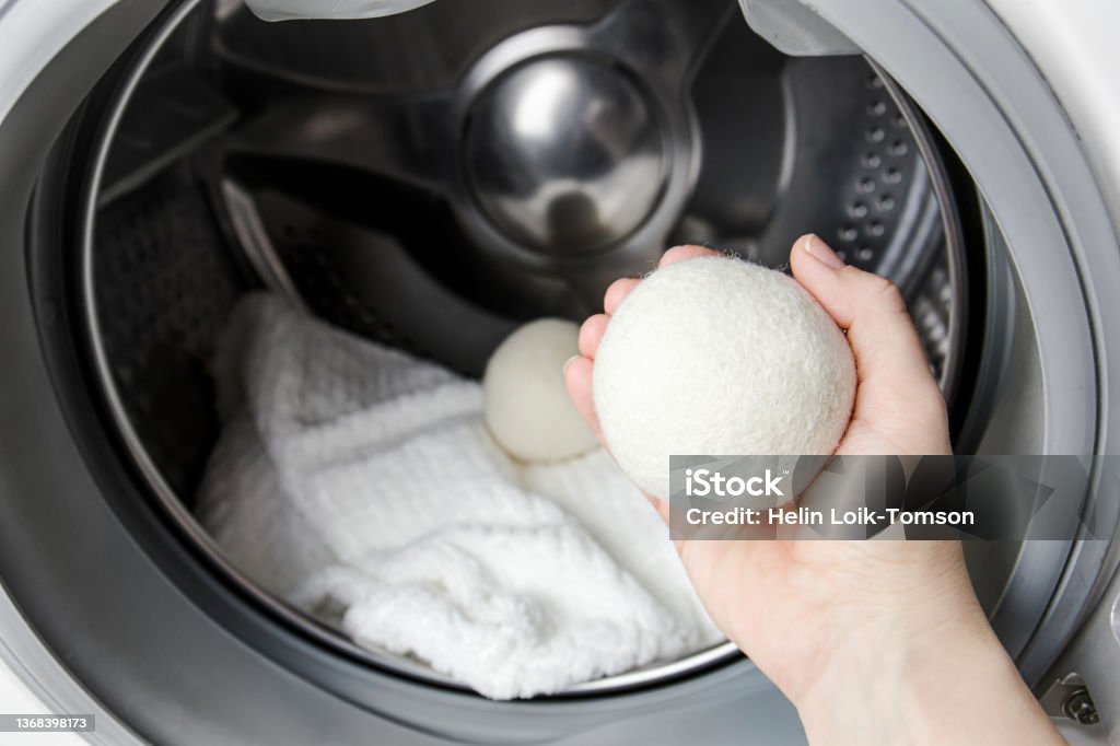 Woman using wool dryer balls for more soft clothes while tumble drying in washing machine concept. Discharge static electricity and shorten drying time, save energy. Dryer Stock Photo