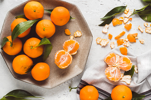 Mandarins (oranges, mandarins, clementines, citrus fruits) with leaves in a plate  on delicate grey background