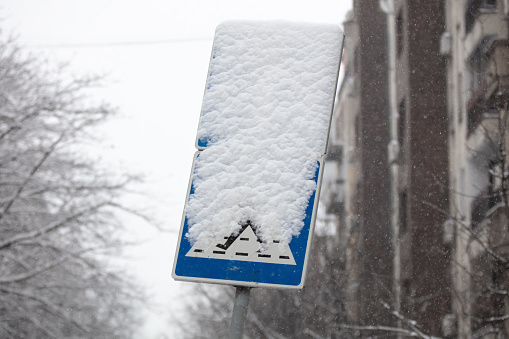 Crosswalk sign for pedestrians covered with snow.