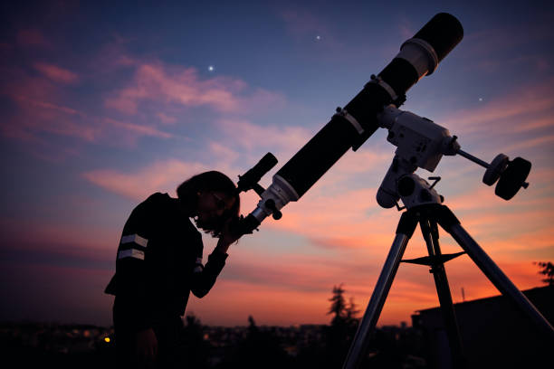 istock Girl with astronomical telescope stargazing under twilight sky. 1368399285