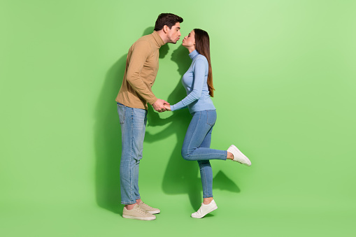 Retrato de perfil de tamaño completo de dos encantadoras personas idílicas que sostienen los brazos besando los labios aislados sobre un fondo de color verde photo