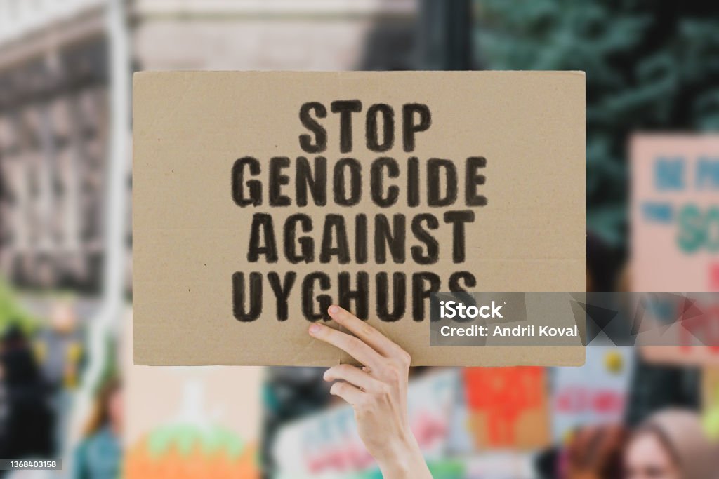 The phrase " Stop genocide against uyghurs " on a banner in men's hand. Human holds a cardboard with an inscription. Communism. Totalitarianism. Kill. Prison. Colonies. Control. Discrimination. Rights Uygur Culture Stock Photo