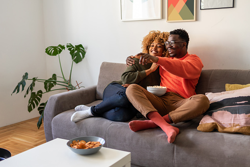 A young African-American couple is enjoying a tv show. The couple looks happy and cheerful.