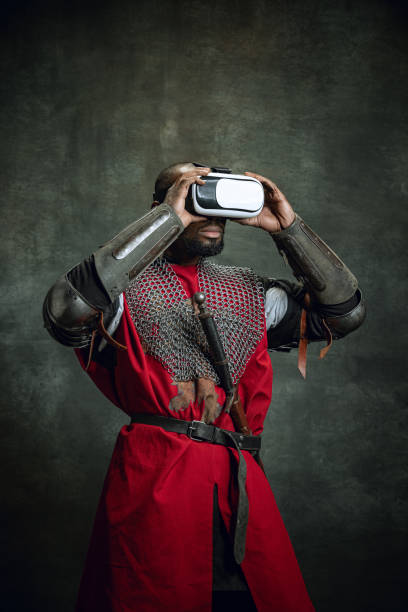 istock Modern gadgets. One dark skinned man, medieval warrior or knight using VR headsets isolated over dark vintage background. Comparison of eras, history, technology 1368411882
