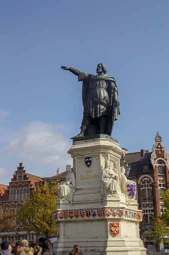 Bruges, Belgium - June 2, 2013: Statue in the middle of picturesque Bruges, Belgium, with colorful flags and buildings in background. Statue of Pieter De Coninck at Market Square in Bruges, Belgium. People are having rest at the cafes around the statue in the Market Square.
