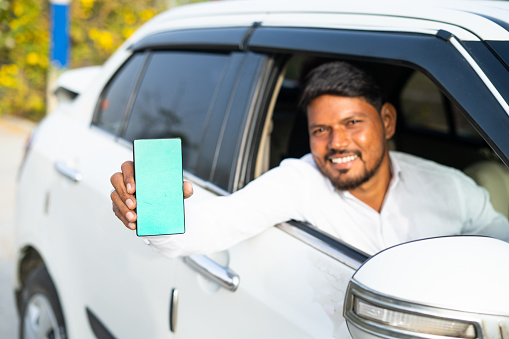 Focus on mobile, cab driver showing mobile phone with green screen mockup by looking at camera - concept of online booking service, app advertising for travel service and promotions.