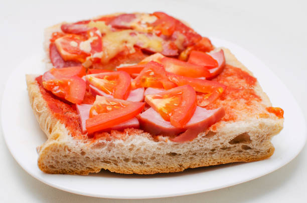 White bread sandwich with sausage, tomatoes and sauce on a white background.