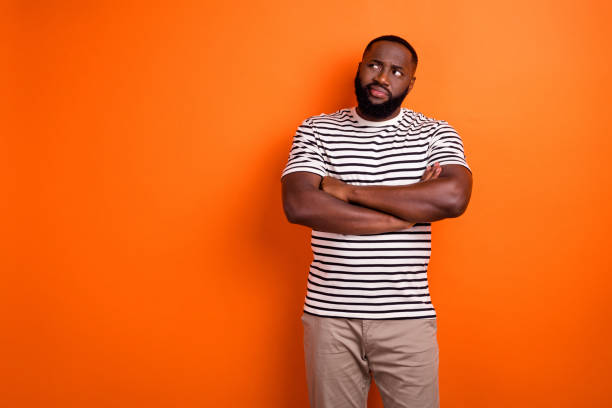 istock Photo of young african man folded hands look empty space thoughtful uncertain isolated over orange color background 1368412596