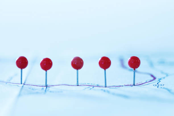 A row of push pins  spaced out on a road map.  The image is photographed with a very shallow depth of field.