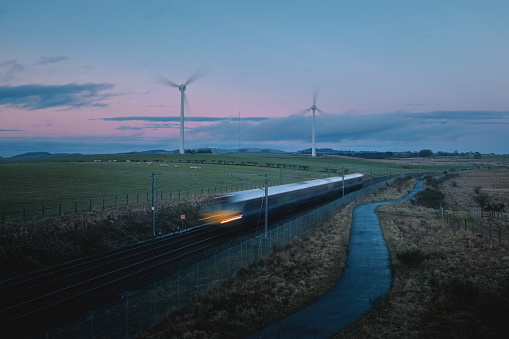 Moving blurred train across countryside and windmills in the field on the background in the evening. Blue hour. West Lothian, Scotland