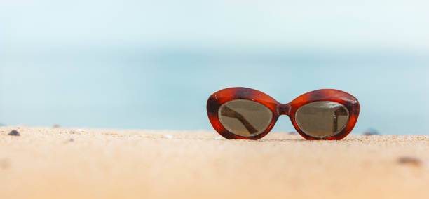 Vintage glasses on a sandy beach with blue sea in the background Vintage glasses on a sandy beach with blue sea in the background sonnenbrille stock pictures, royalty-free photos & images
