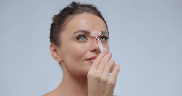 istock Beautiful woman using stone facial roller over gray background. Young model having perfect smooth skin. 1368414510
