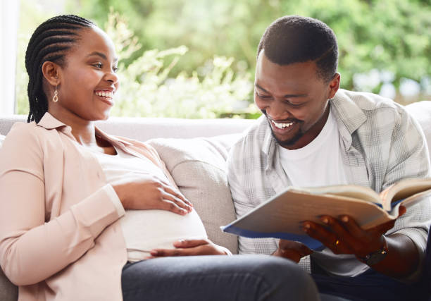 Cropped shot of a handsome young man reading a book to pregnant wife's belly while sitting on the sofa at home Story time real wife stories stock pictures, royalty-free photos & images
