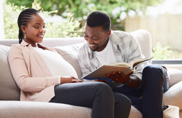 Cropped shot of a handsome young man reading a book to pregnant wife's belly while sitting on the sofa at home Let me read you a story real wife stories stock pictures, royalty-free photos & images