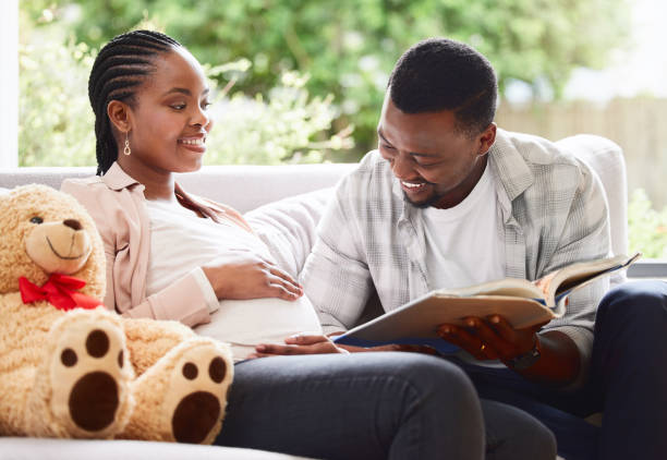Cropped shot of a handsome young man reading a book to pregnant wife's belly while sitting on the sofa at home He loves reading to his unborn baby real wife stories stock pictures, royalty-free photos & images