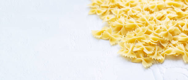baner surowego włoskiego makaronu farfalle na białym stole - bow tie pasta italian cuisine bow heap zdjęcia i obrazy z banku zdjęć