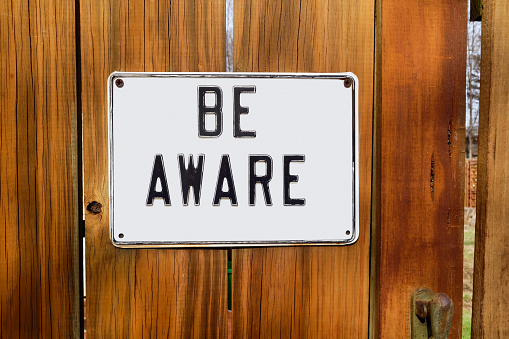 Metal BE AWARE concept sign mounted on wooden fence with gate ajar.
