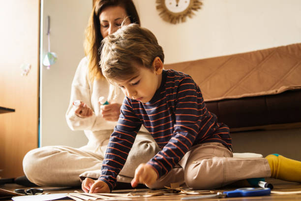 Mother and son playing at home having fun in room cutting paper with scissors making craft and art toys developing skills - childhood and development learning new skills family leisure concept madre e hijo jugando en casa divirtiéndose en la habitación cortando papel con tijeras haciendo manualidades y juguetes de arte desarrollando habilidades - infancia y desarrollo aprendizaje de nuevas habilidades concepto de ocio familiar