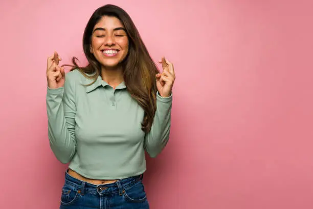 Hopeful woman with her fingers crossed feeling lucky and praying for her wishes to come true