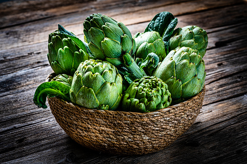Close up view of fresh organic artichokes in a basket shot on rustic wooden table. High resolution 42Mp studio digital capture taken with SONY A7rII and Zeiss Batis 40mm F2.0 CF lens