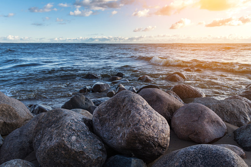 Photo of the rocky shoreline of the Finland Bay of Baltic Sea in St. Petersburg at sunset. Rocks located on the beach. against the background of a choppy sea and a cloudy sky