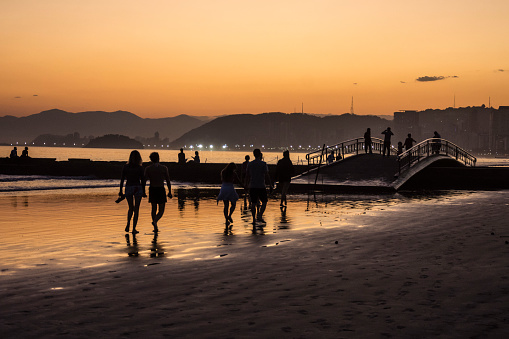 People walking on the beach, crossing the canal by the bridge and enjoying the sunset in the city of Santos, Brazil.
