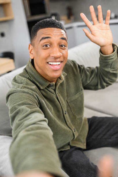 istock Video communication, zoom. Multiracial young guy waving hello to the smartphone camera, while preparing to conversation 1368427475