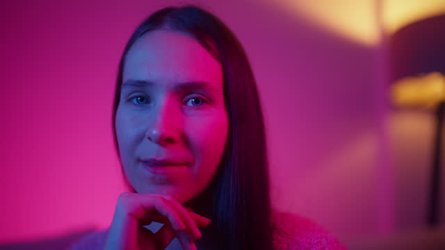 Portrait of beautiful woman lit by pink and blue lights sitting on sofa