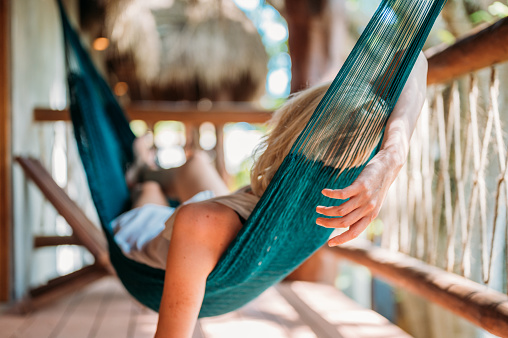 Rear view of a woman relaxing in a hammock hanging on the balcony of a beautiful eco wooden house