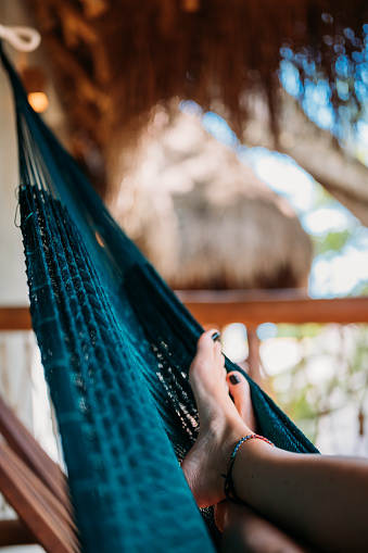 Close-up of woman's feet during her relaxing summer day in hammock on the balcony of a beautiful eco wooden house   
Travel, leisure and vacation concept