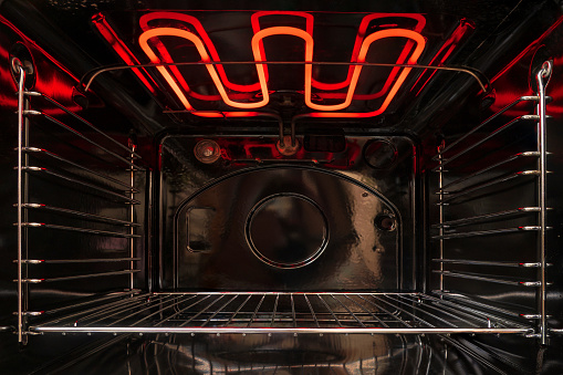 Mirando dentro del horno de cocina vacío negro. Hay un estante de celosía y un elemento calefactor al rojo vivo. Fondo. photo