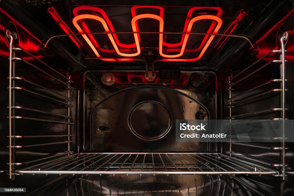 Looking inside the black empty kitchen oven. There is a lattice shelf and a red hot heating element. Background. Oven Stock Photo