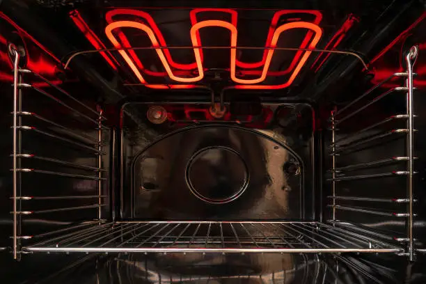 Photo of Looking inside the black empty kitchen oven. There is a lattice shelf and a red hot heating element. Background.