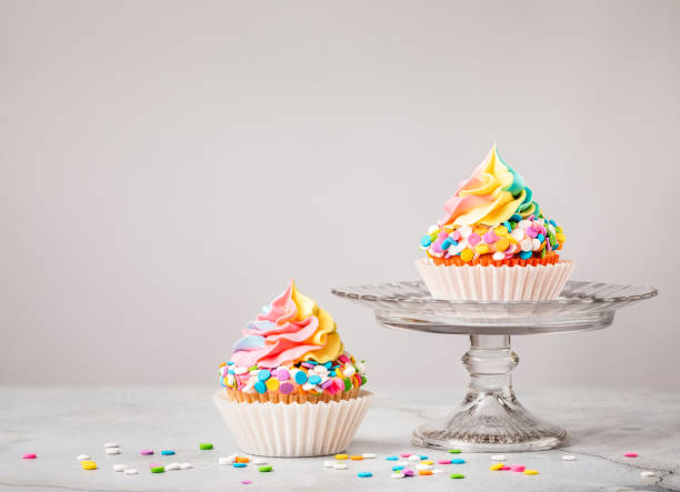 Rainbow Birthday Cupcakes with Sprinkles Two Rainbow Birthday cupcakes with colourful sprinkles over light grey background. version 2 stock pictures, royalty-free photos & images