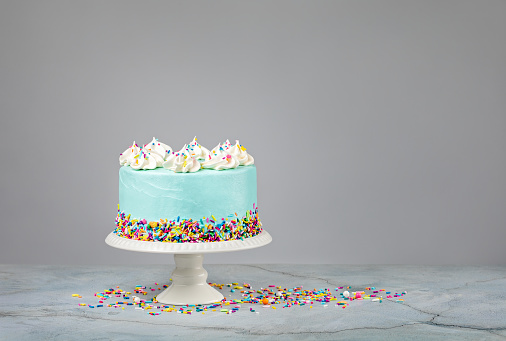 Blue Birthday Cake with colourful sprinkles over a light grey background.