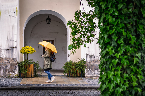 Woman with yellow umbrella walking at city street in rain. Female tourist walks in European old town Kromeriz, Czech Republic