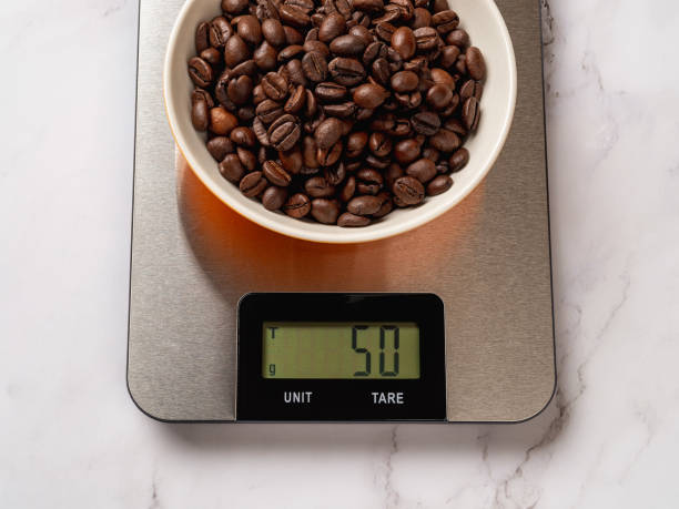 Roasted coffee beans in a bowl on a digital kitchen scale. The scales displaing 50g of coffee beans without tare. Electronic metallic device for measurement the food weight for dieting and cooking. stock photo