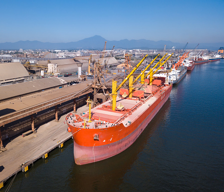Drone aerial view of red bulk carrier cargo ship loaded with soy at sea port on sunny summer day. Concept of logistics, commerce, economy, industry, transport, vessel, transportation.
