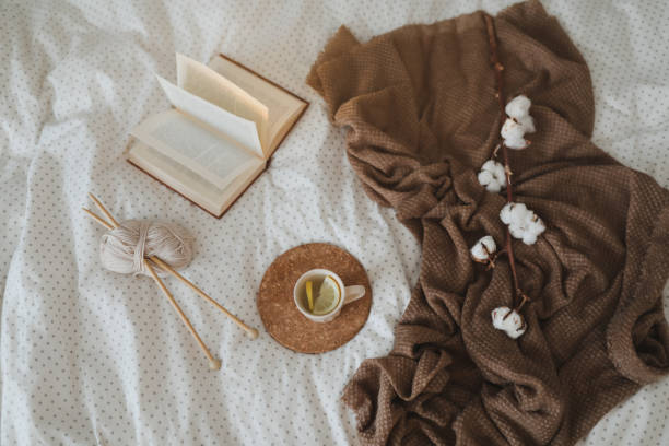 istock Cozy winter background with a book, tea cup and knitting needles in warm soft bed top view. Sweet home. 1368447267
