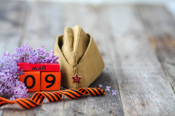 Wooden calendar with Russian text May 9, garrison cap, george ribbon and a bouquet of lilacs on a wooden background. Victory Day. Wooden calendar with Russian text May 9, garrison cap, george ribbon and a bouquet of lilacs on a wooden background. Victory Day. 1945 stock pictures, royalty-free photos & images