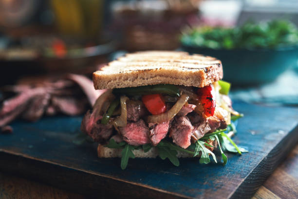 A close up shows a wagyu style steak sandwich with rare beef in toasted bread, parsley on top, plus a paper cup of fries and snacks, street food style in Tokyo.
