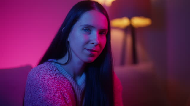 Portrait of beautiful woman lit by pink and blue lights sitting on sofa